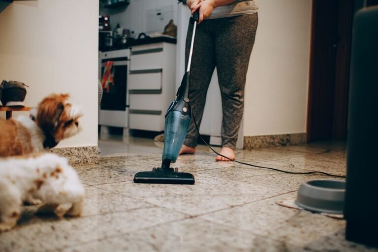 A dog watching someone vacuum a tiled living room floor