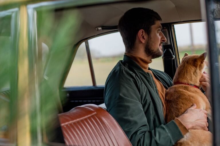 A man sitting in the back seat of a car holding his dog
